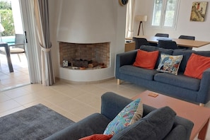 A living room with a fireplace, a sofa, a coffee table, and a dining area with chairs.