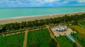 Vista sulla spiaggia, cielo sereno, spiaggia sabbiosa e area verde con alberi e un padiglione.