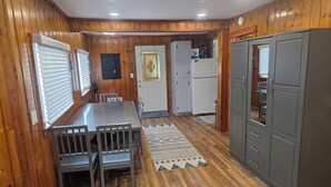 Una cocina compacta con paredes de madera, un comedor con mesa y sillas, un refrigerador y una alfombra estampada.