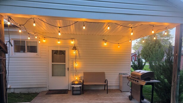 Un patio cubierto con luces colgantes, una parrilla y un banco.