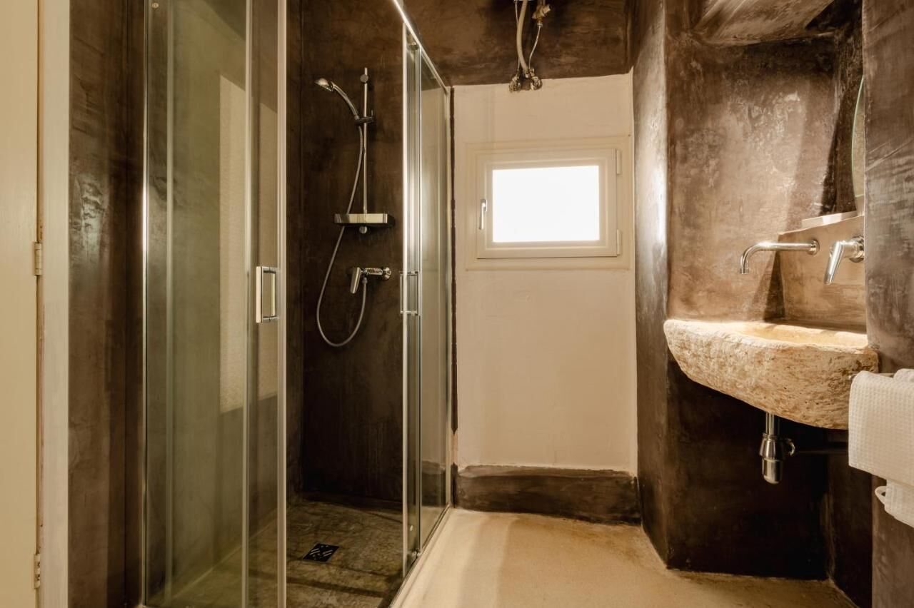A modern bathroom with a glass-enclosed shower, a stone sink, and a small window providing natural light.