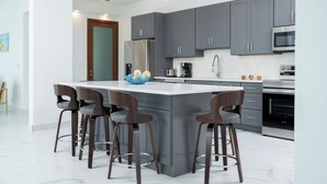 Una cocina moderna con armarios grises, una isla grande con taburetes de bar, electrodomésticos de acero inoxidable e iluminación colgante.