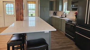 A kitchen with a large island, dark cabinets, and a stainless steel refrigerator.
