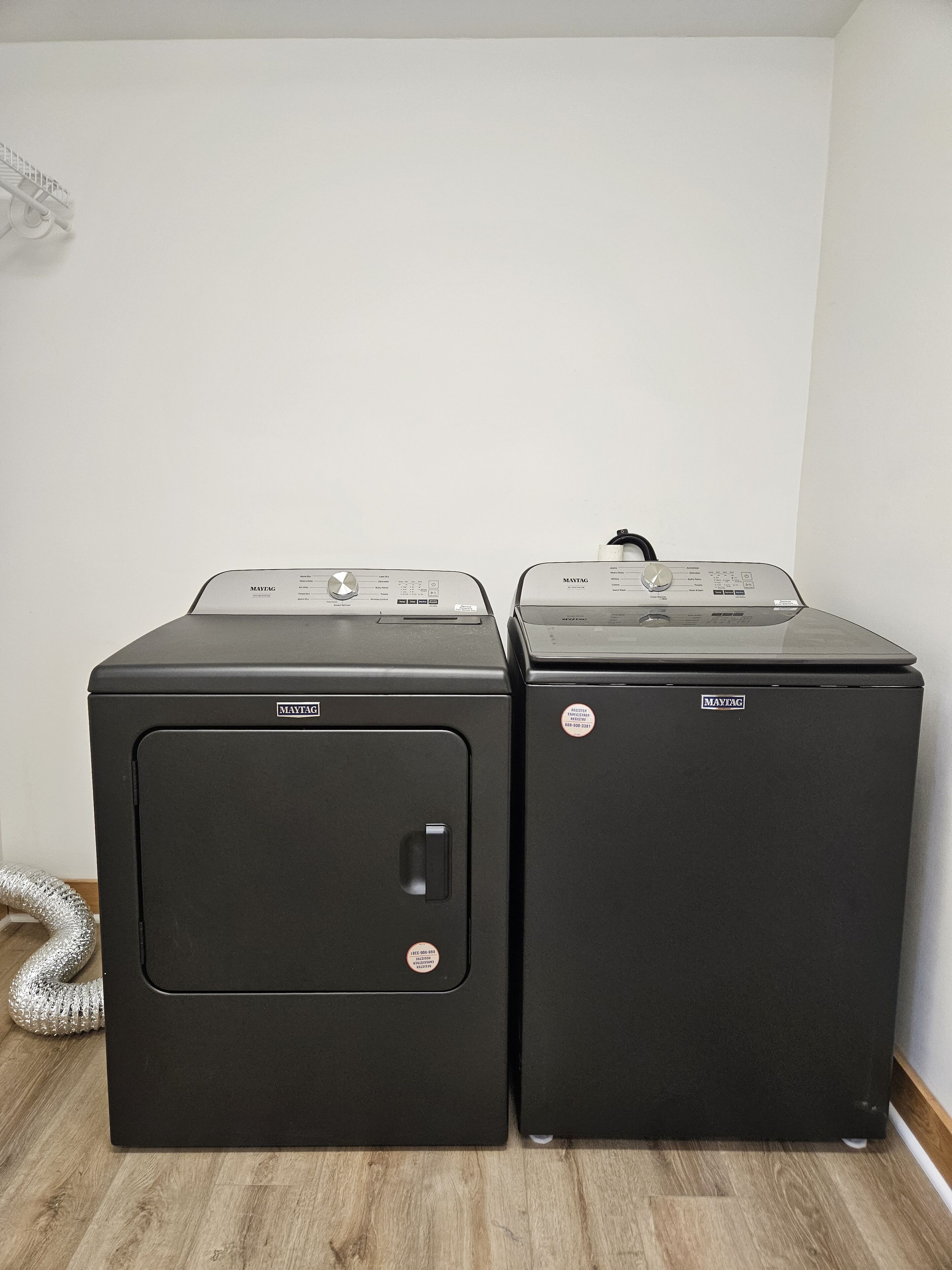 Two black Maytag front-loading washing machines in a room with wooden flooring and a white wall.