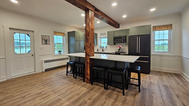 A spacious kitchen with a central island, wooden flooring, and a view of the outdoors through large windows.