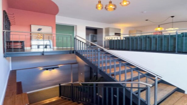 Een modern interieur met een trap, metalen leuningen en hanglampen.