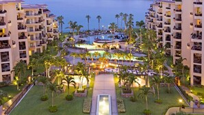 Un resort con varias edificaciones, un área de piscina central y vista al mar.