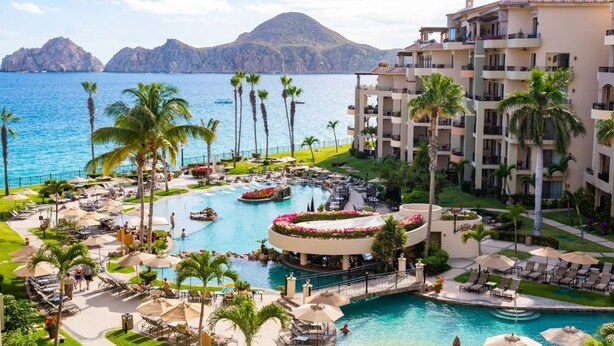 Un resort con una piscina grande, palmeras y vistas al mar.