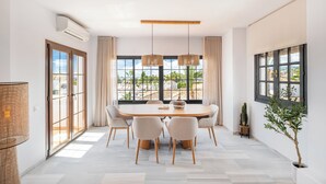 A dining area with a large table, four chairs, and a view of a residential area through large windows. - Luxurious 3BDR apartment Puerto Banús, Marbella (Marbella)