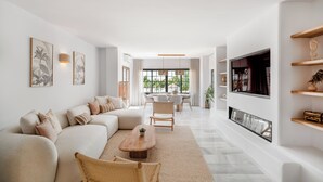A modern living room with a sofa, a coffee table, and a TV mounted on the wall. There is a dining area with a table and chairs in the background. - Luxurious 3BDR apartment Puerto Banús, Marbella (Marbella)