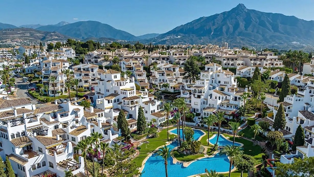 A resort with white buildings, a central swimming pool, and a mountain in the background. - Luxurious 3BDR apartment Puerto Banús, Marbella (Marbella)
