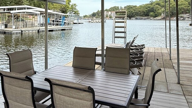 Un espace extérieur abrité, avec une table et des chaises, offrant une vue sur une étendue d’eau où l’on aperçoit des bateaux et des quais au loin.