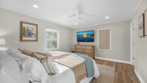 Une chambre à coucher avec un lit, une commode, un téléviseur et une fenêtre avec des stores.