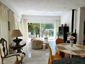 A spacious room with a large window, a dining table, a sofa, and a decorative cabinet.