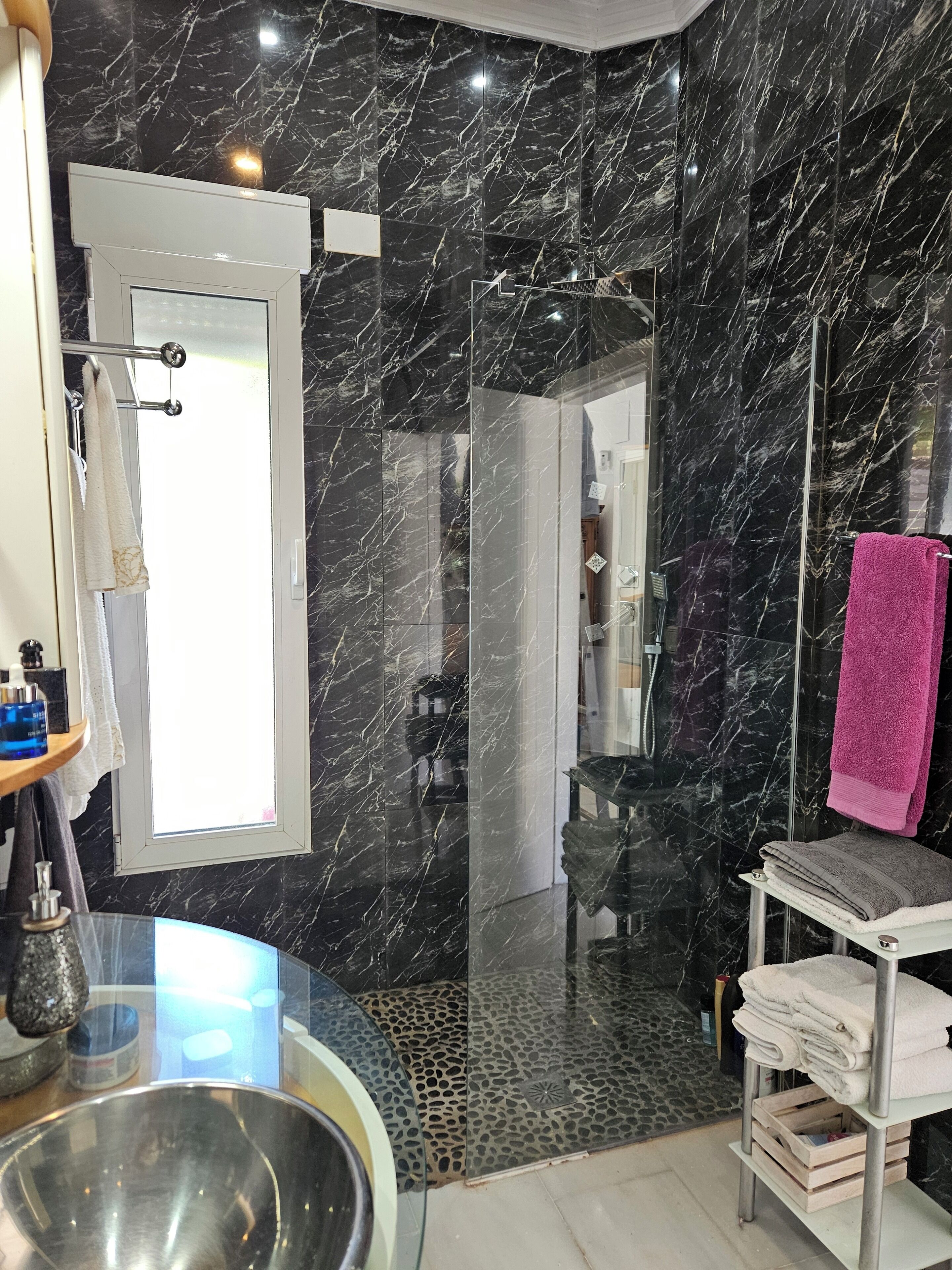 Une salle de bain moderne dotée d’une douche à parois de verre, de murs en marbre et d’une porte visible donnant sur une autre pièce.