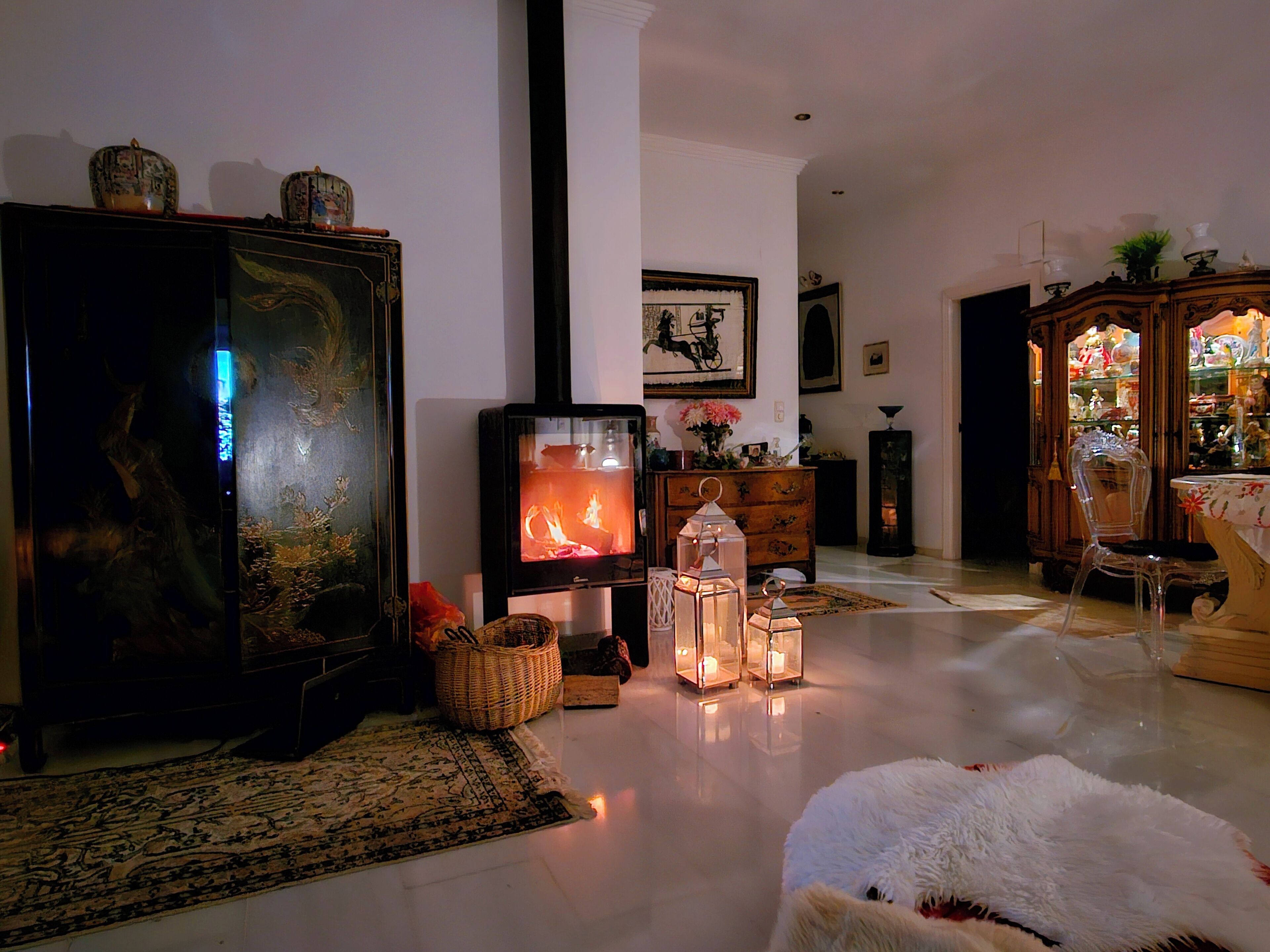 A cozy living room with a fireplace, a large cabinet, and a clear chair.