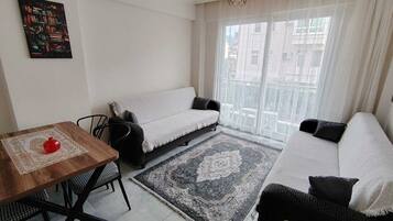 Un salon moderne avec un canapé, une table à manger et des chaises, un tapis et une grande fenêtre avec des rideaux.