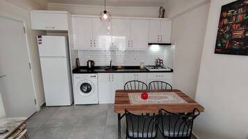 Une cuisine compacte avec des meubles blancs, un lave-linge, une table à manger avec des chaises et un luminaire suspendu.