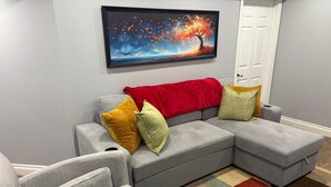 Un soggiorno moderno con un divano angolare grigio, due poltrone, un tappeto colorato e un grande quadro raffigurante un albero.