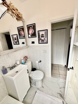 A bathroom with a white sink, toilet, and marble floor. There are framed pictures on the wall and a decorative plant on the counter.