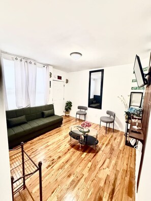 A living room with a green sofa, a round coffee table with flowers, two grey chairs, and a wooden floor.