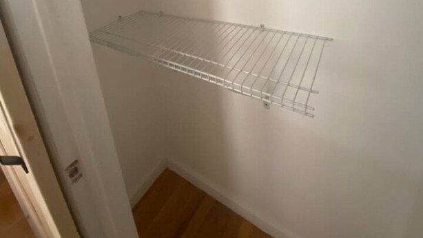 A small, empty walk-in closet with a metal shelf and a white hanger. - Comfy Getaway Private Apt Studio (West New York)