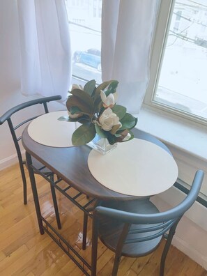 Ein runder Esstisch mit zwei Stühlen, eine Vase mit Blumen und ein Fenster mit Vorhängen.