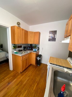 A compact kitchen with wooden cabinets, a microwave, a coffee maker, and a small sink.