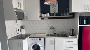 A compact kitchen with a washing machine, a sink, and a microwave. - Modern Sea Side Studio, a Surfer, Beach Goer or Cape Town Explorer's Paradise (Cape Town)