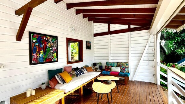 A covered porch with wooden flooring, a bench, a sofa, and a small table. There are two framed artworks on the wall. - KAY BLUE Creole house in the heart of nature, 2 steps from the beaches, magnificent (Les Trois-Îlets)