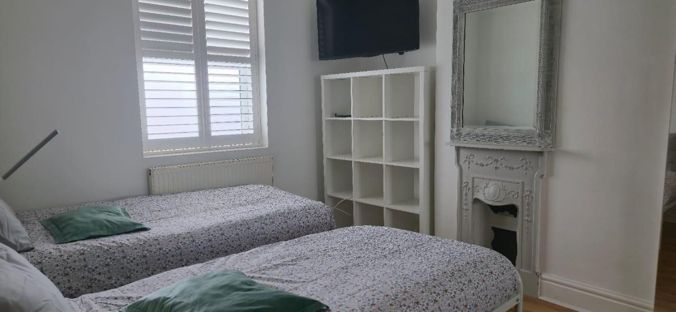 A bedroom with two beds, a white radiator, a TV mounted on the wall, and a fireplace.