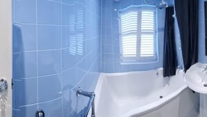 Un baño con azulejos azules, una bañera, dos lavamanos y una ventana con persianas.