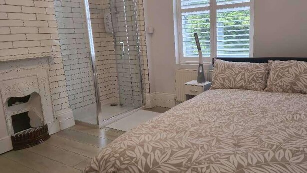 Un dormitorio con cama, zona de ducha y chimenea.