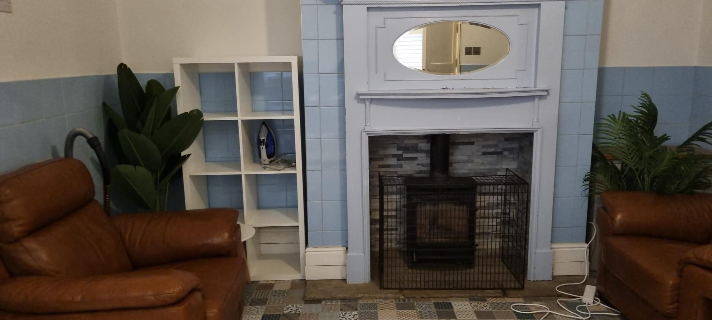 A living room with a fireplace, two leather sofas, a white shelving unit, and a large mirror above the fireplace.