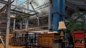 An industrial-style interior with exposed beams, a wooden floor, and a mix of bar stools and a wooden cabinet. - The Texas Bluebonnet, Historic Downtown McKinney Area! (McKinney)