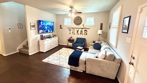A living room with a flat-screen TV, a ceiling fan, a sofa, a coffee table, and a rug. - The Texas Bluebonnet, Historic Downtown McKinney Area! (McKinney)