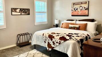 A bedroom with a cow print bedspread, a nightstand with a lamp, and a wall-mounted artwork depicting a bar scene.