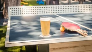 A table with a glass of beer and a table tennis paddle, set outdoors with string lights in the background. - The Texas Bluebonnet, Historic Downtown McKinney Area! (McKinney)