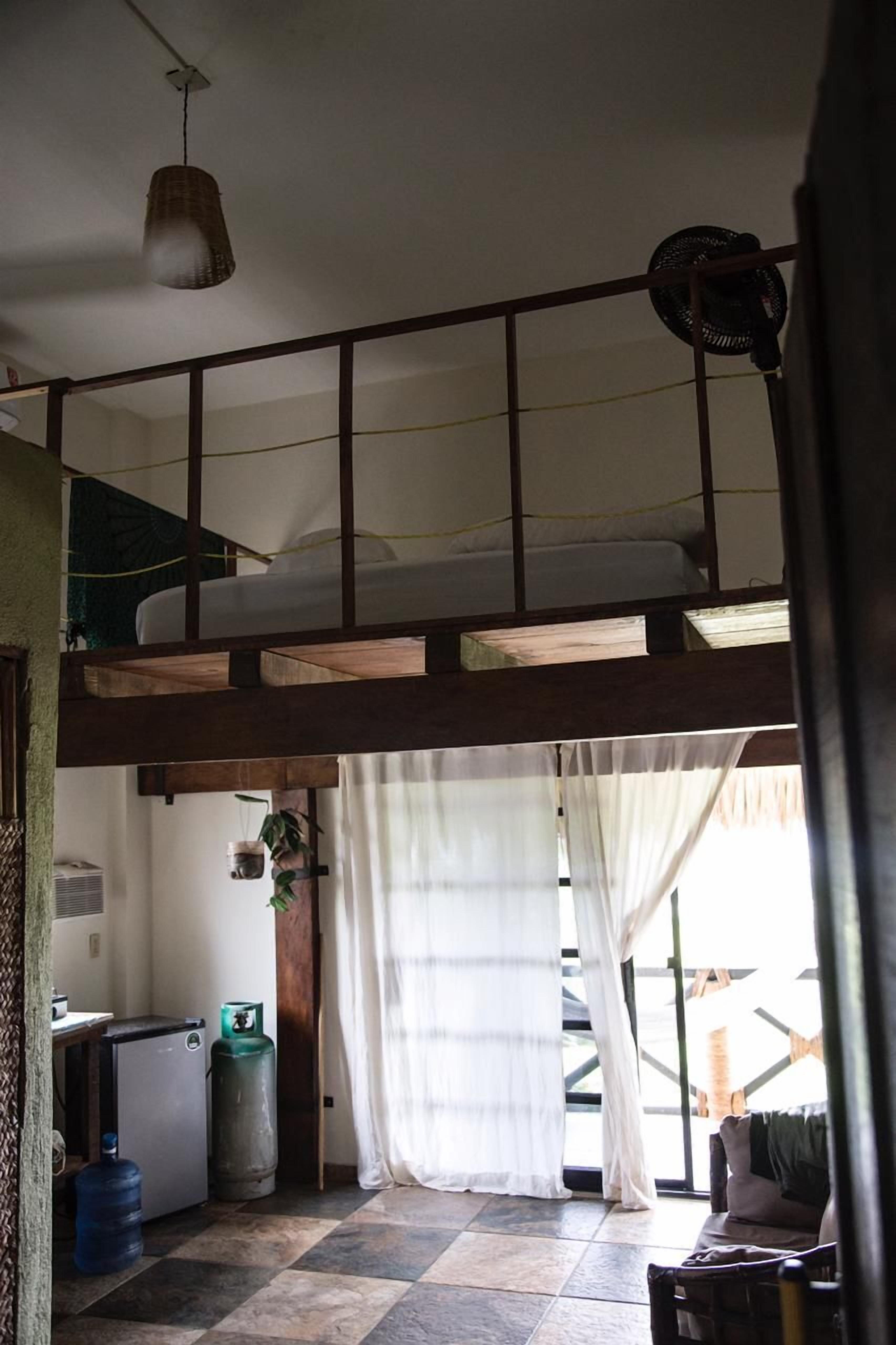 Habitación con cama tipo litera, kitchenette pequeño, dispensador de agua y una ventana grande con cortinas.