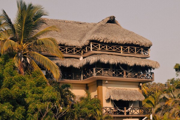 A multi-story building with thatched roofs and wooden railings, surrounded by lush greenery. - Beachfrontguesthouse (Puerto Escondido)