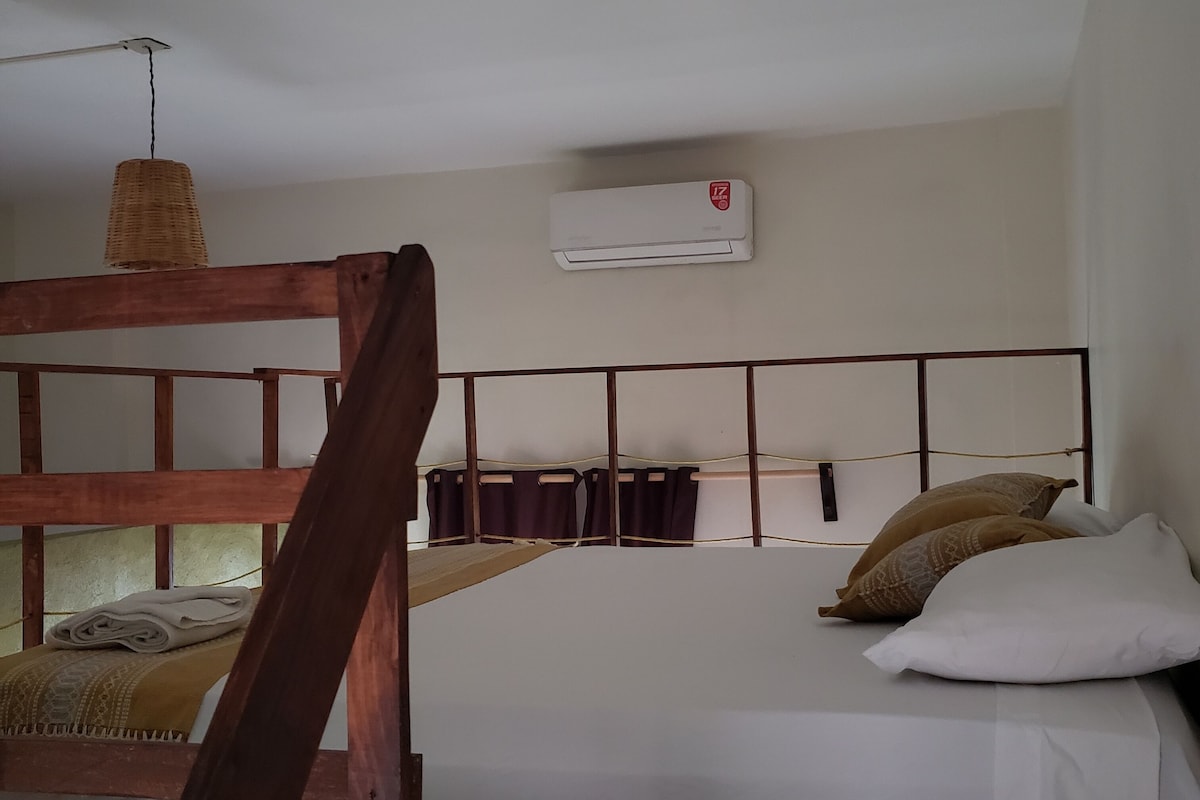A bunk bed with a wooden ladder, a white bed with two pillows, a woven light fixture, and an air conditioning unit on the wall.