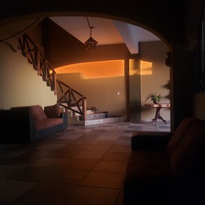 A spacious living area with a staircase, a sofa, and a small table with a plant. - Beachfrontguesthouse (Puerto Escondido)