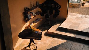 Une pièce dotée d’un sol carrelé, d’une table en bois ornée d’une plante, d’un luminaire suspendu et d’une étagère contenant des livres et des objets décoratifs.