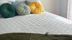 A bed with a patterned white cover, three pillows in green, grey, and yellow, and a painting above the bed. - Located Midway Orlando & Daytona Beach, Pet Friendly, Fenced Yard, 2 Car Garage (Deltona)