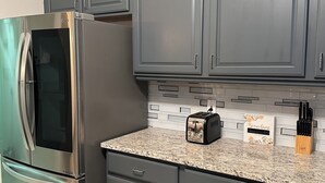 A kitchen with dark cabinets, a stainless steel refrigerator, a toaster, and a knife block on the countertop. - Located Midway Orlando & Daytona Beach, Pet Friendly, Fenced Yard, 2 Car Garage (Deltona)