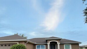 A single-story house with a front garage, a well-maintained lawn, and a clear sky. - Located Midway Orlando & Daytona Beach, Pet Friendly, Fenced Yard, 2 Car Garage (Deltona)