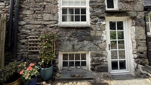 Un edificio de piedra con tres ventanas, una puerta y un pequeño porche.