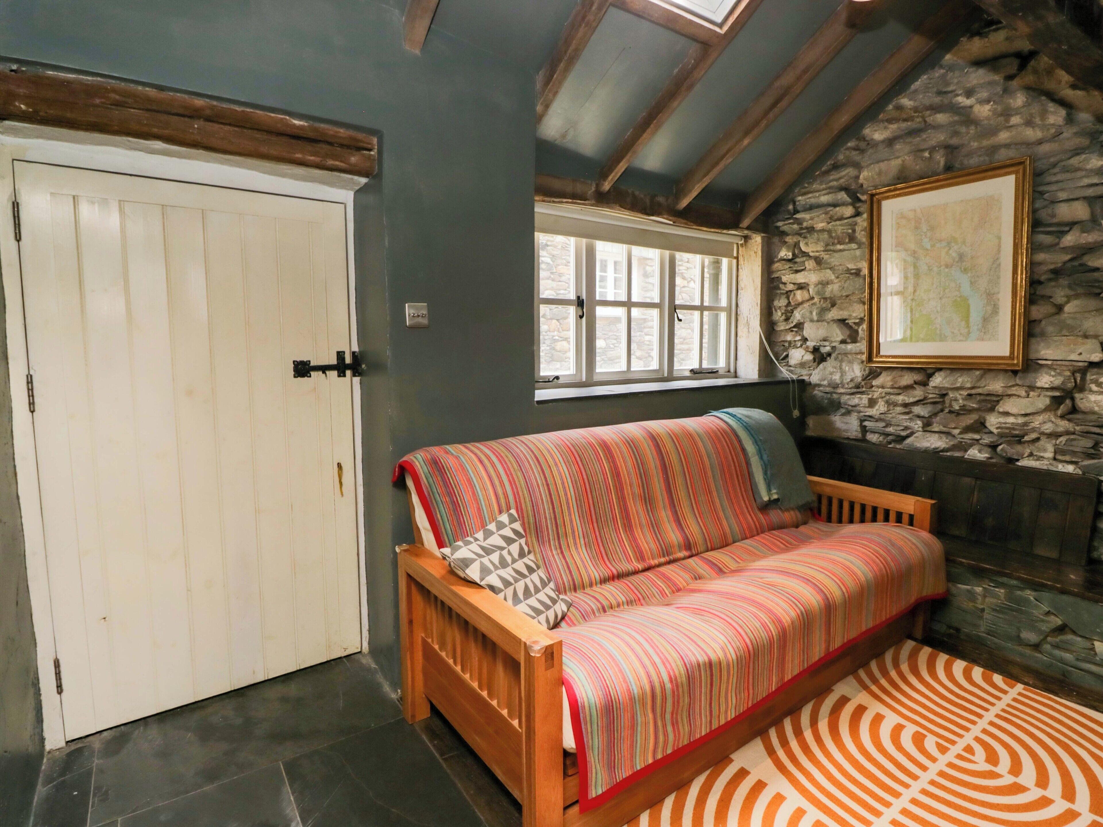 A cozy room with a wooden sofa, a white door, a stone wall, and a window.