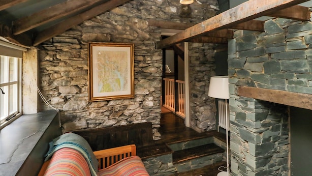 Una habitación acogedora con pared de piedra, un banco de madera, una lámpara colgante y un mapa enmarcado en la pared.