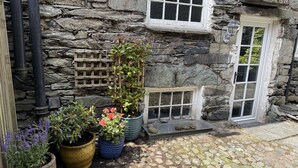 Un edificio de piedra con una valla de madera, una ventana con marco blanco y plantas en macetas.